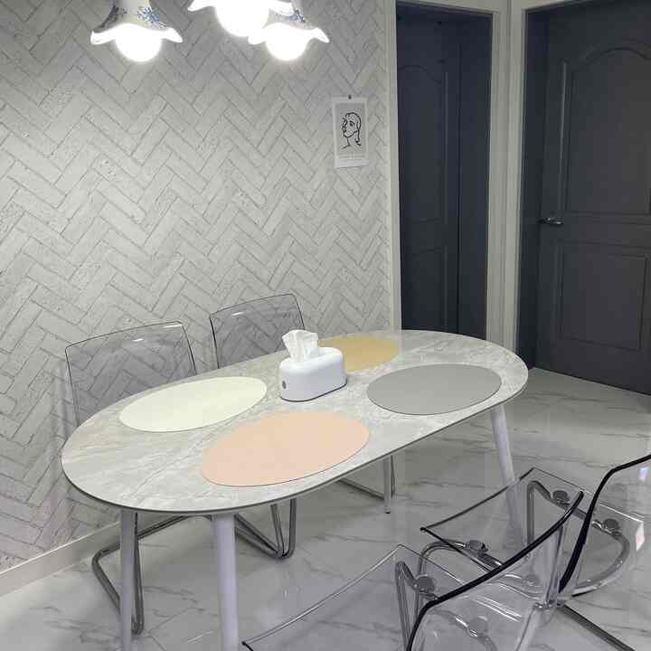 ホワイトとグレーの色調のダイニング、透明な椅子と大理石調の楕円形テーブルに4つのランチョンマットが配置されたモダンな空間