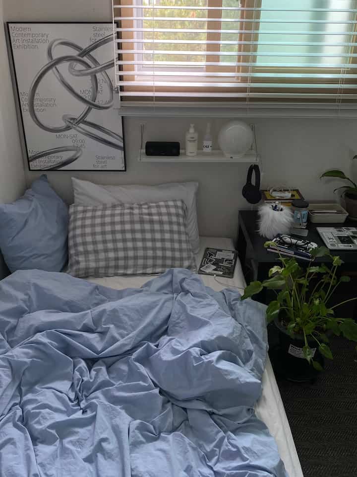 Calm blue and white toned bedroom featuring a simple bed, side table, and plants in a modern setting