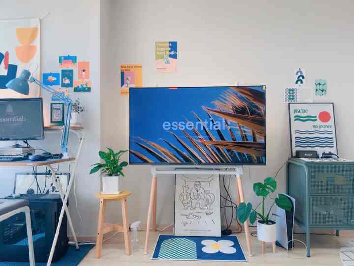 A blue-toned studio apartment featuring a modern TV stand, stool, desk, and plants in a cozy arrangement