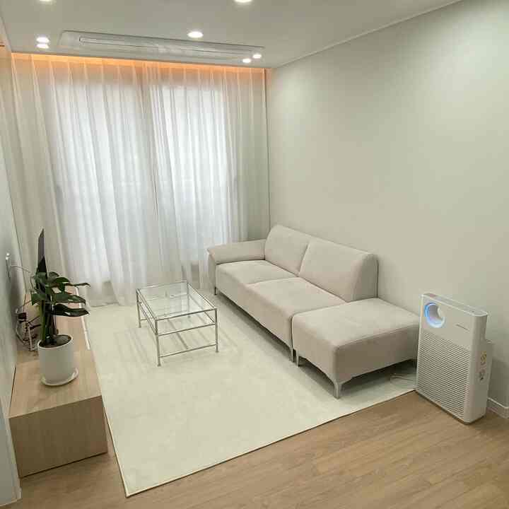 明るいホワイトとナチュラルウッドが調和する狭くコンパクトなリビング、ベージュのソファと透明なコーヒーテーブルが配置された清潔感のある空間