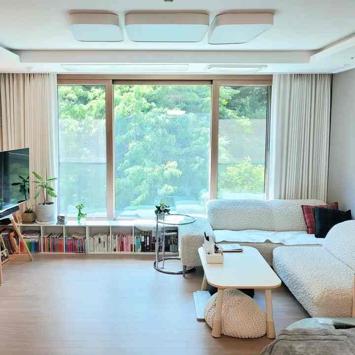 Beige and white toned living room featuring bookshelves by the window and white sofas with a table in a natural modern style