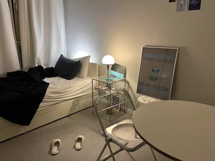 柔らかな照明と透明な椅子が配置されたモダンな6坪ワンルームの寝室とダイニングスペース