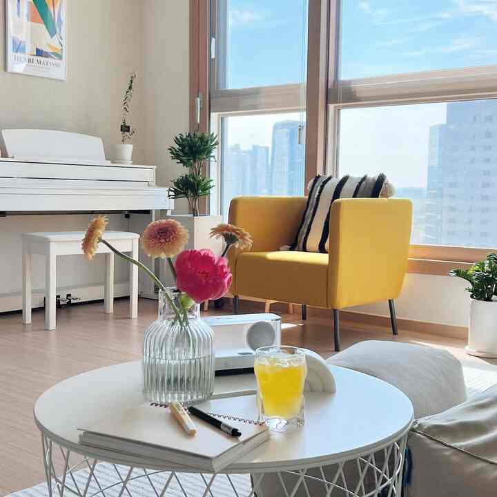 White and yellow toned living room featuring a yellow armchair, vase with flowers, and large windows in a clean modern space