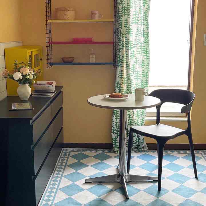 Cozy small dining space with yellow-toned walls, black dresser, round white table, and green patterned curtains