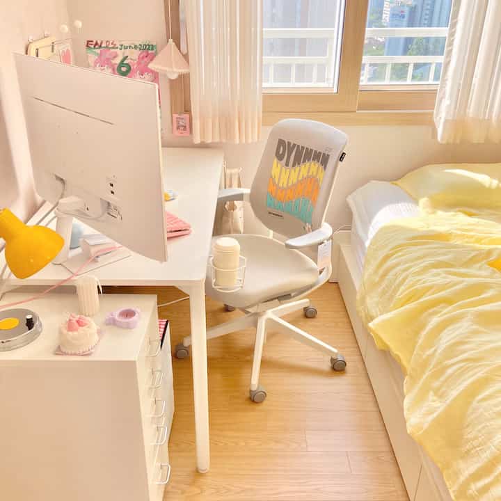 明るく自然な木目調の床と白い家具が調和した一人暮らし用の書斎兼寝室空間、黄色い布団がアクセントの居心地の良い部屋