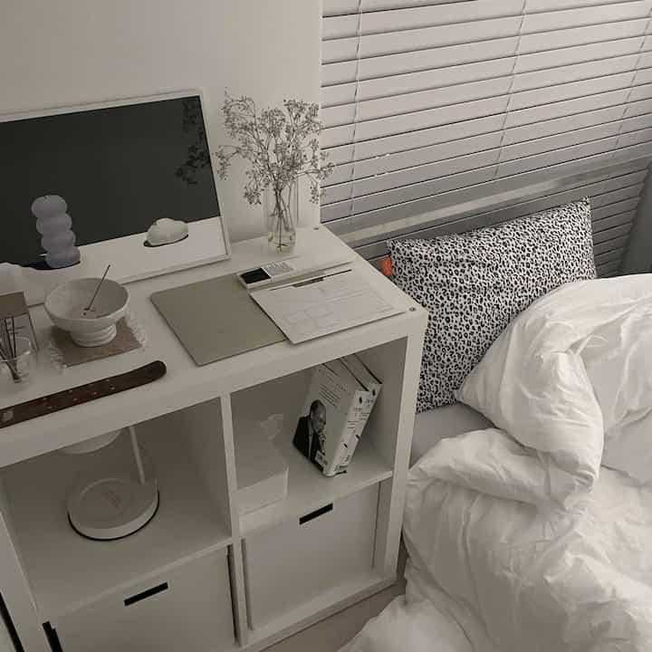 White-toned bedroom featuring an IKEA shelving unit and leopard print pillow with a simple modern atmosphere