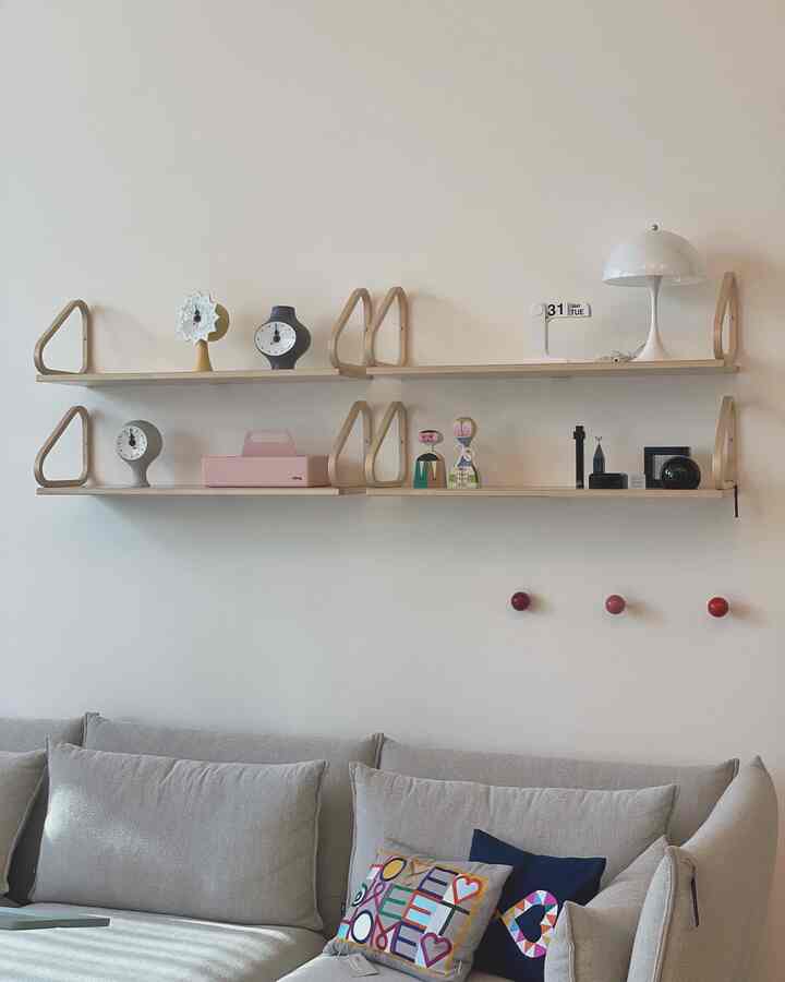 ベージュとナチュラルカラーのリビング、クッションと複数の時計が置かれた壁棚が配置された落ち着いた空間