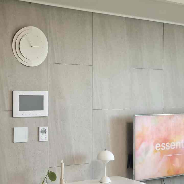 グレーの壁パネルと白い壁時計、テレビやテーブルランプが配置されたモダンなリビング空間