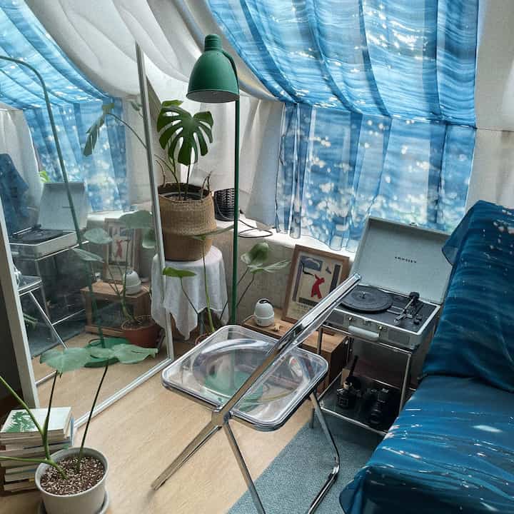 Living room with blue curtains and fabric posters, featuring transparent chair and green floor lamp creating a natural, cozy vibe