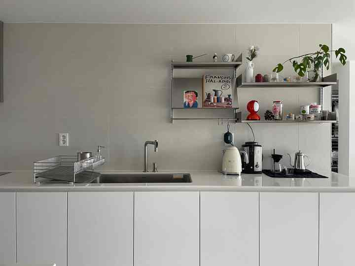 白とステンレス調の上部キャビネットなしのキッチン、レアロウのステンレス棚とキッチン家電が配置されたモダンな空間