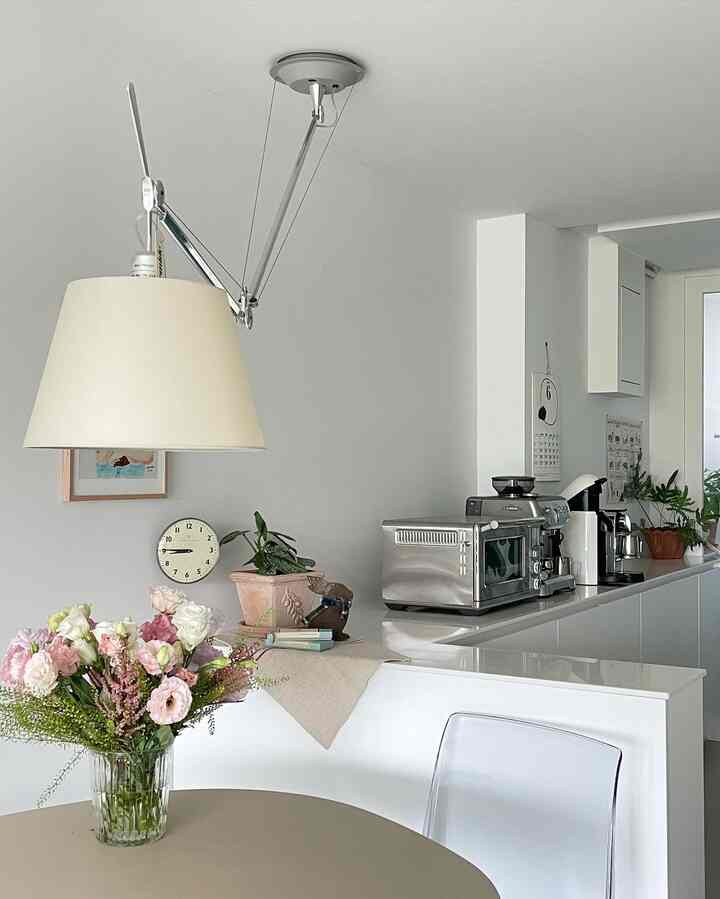 White-tone kitchen space featuring an Artemide pendant lamp and coffee machines with clean, modern interior design
