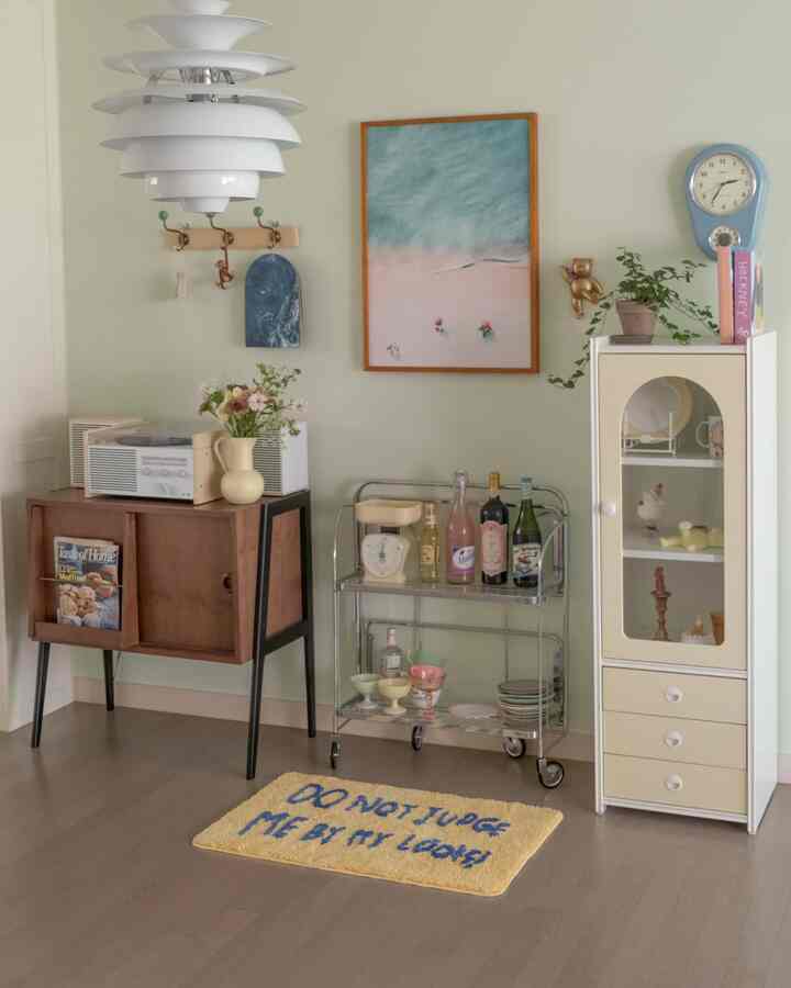 Soft green-toned living room featuring vintage wooden cabinet, metal bar cart, and charming decor creating cozy ambience