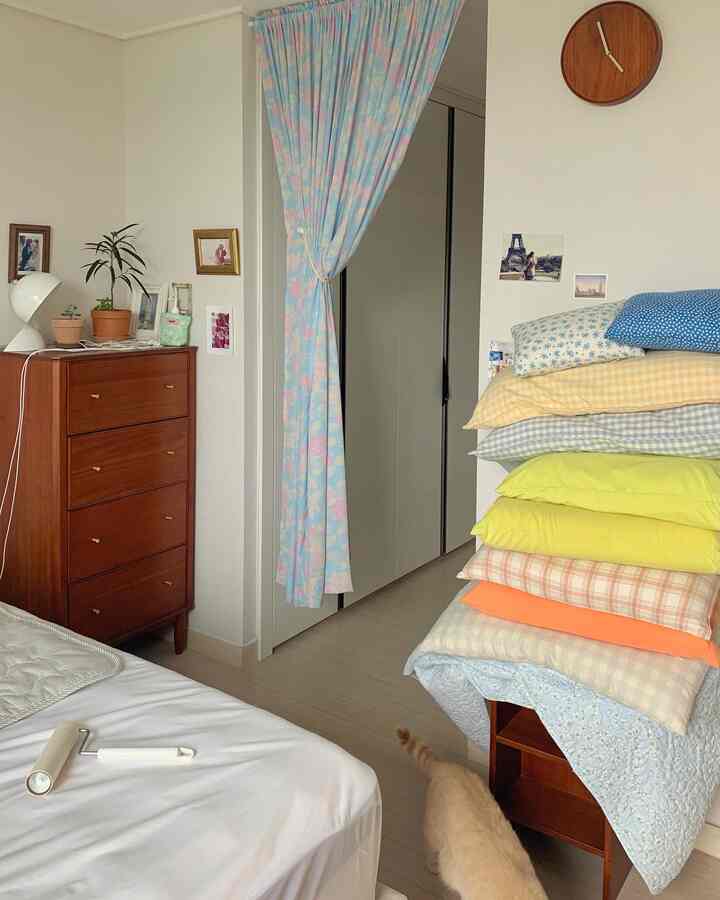 A cozy bedroom with pastel and wood tones featuring a stack of colorful pillows and natural wooden furniture