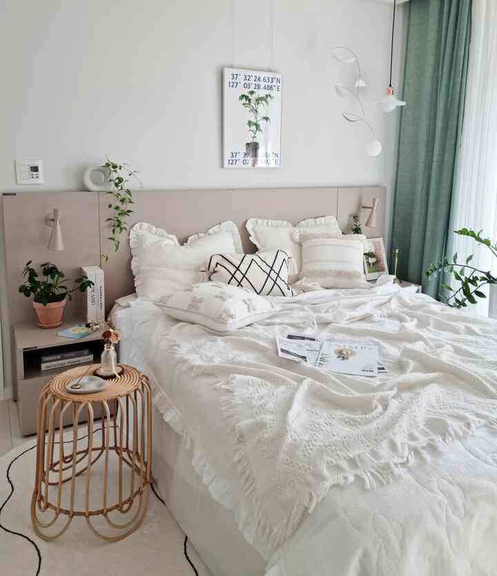 白と明るい緑のトーンの寝室、白い寝具とラタンのスツール、植物のポスターとカーテンが調和したナチュラルな雰囲気のインテリア