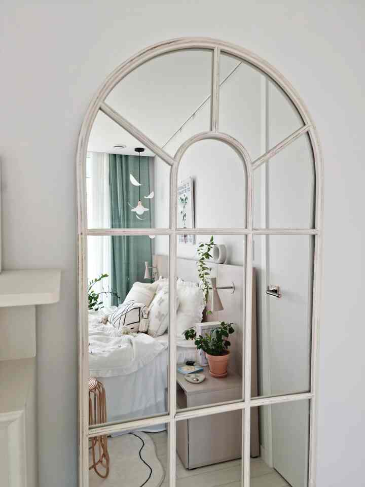白と緑の色調の寝室、ヴィンテージ風のアーチ型鏡と自然な植物が配置された雰囲気のあるインテリア
