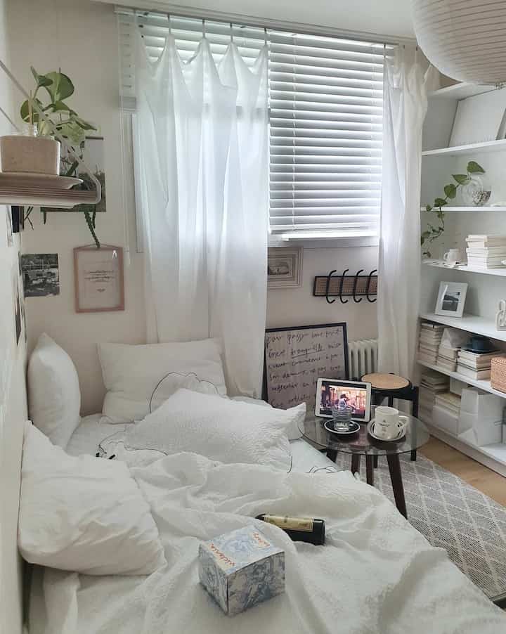 Bright white-toned compact and cozy bedroom featuring a bed and bookshelf with a natural atmosphere