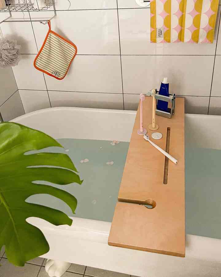 White tiled bathroom featuring a bathtub with a wooden bath tray and green plant, creating a natural vibe