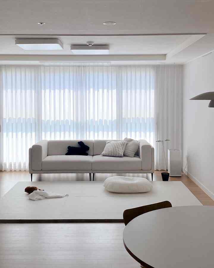 Bright white-toned living room featuring a beige sofa and baby mat with a simple, clean interior