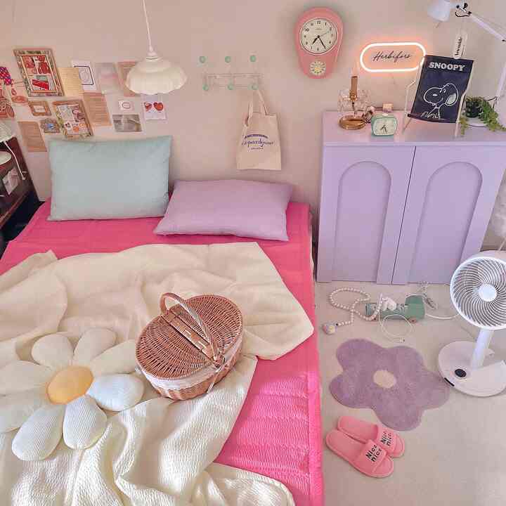 Natural beige-toned bedroom featuring pink bed and cushions, a rattan basket, retro clock, and a table lamp creating cozy atmosphere