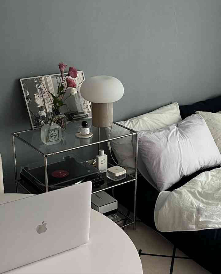 Gray-walled studio bedroom with white round table and mattress, featuring a table lamp and vase decoration creating a cozy atmosphere