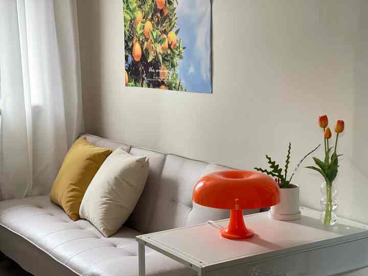 White and beige toned living room featuring a beige sofa with yellow and orange accent cushions and an orange table lamp creating a cozy atmosphere