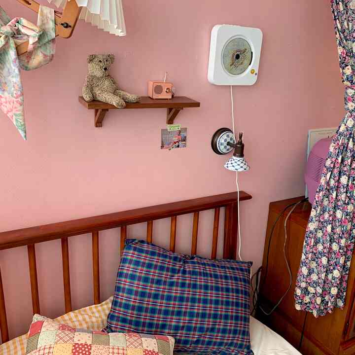 Cozy bedroom with pink walls, wood tone bed, patterned curtain, and wall sconces