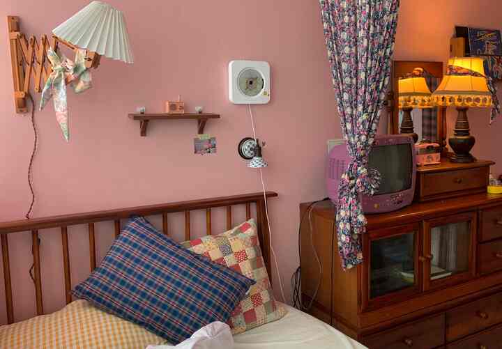 Warm red-toned bedroom featuring wooden furniture, vintage purple CRT TV, and floral curtains creating a cozy atmosphere