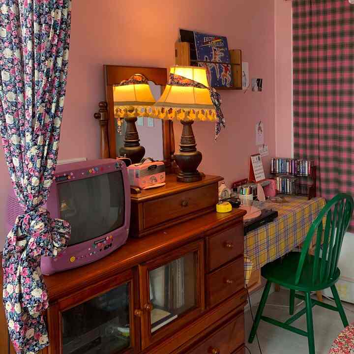 ピンク色の壁と花柄カーテンがあるヴィンテージスタイルの空間、木製家具とレトロな小物が配置された雰囲気のあるインテリア