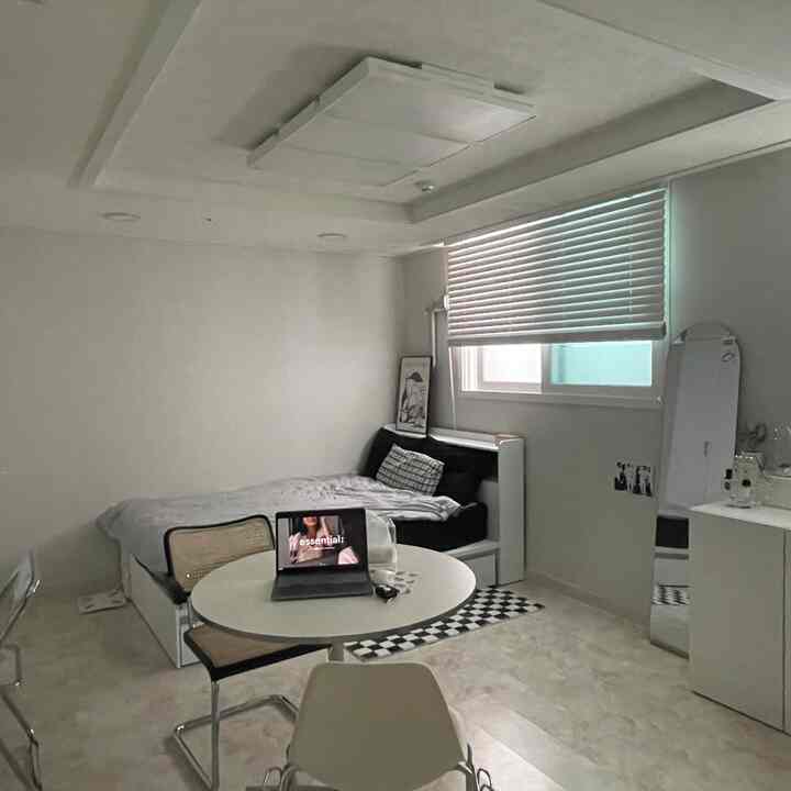 Modern 8-square-meter studio bedroom in white and black tones featuring a round dining table, shelves, and blinds with a simple atmosphere