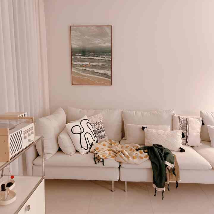 白を基調としたリビング、広々としたソファと壁掛けの絵、ミルクシフォンカーテンが調和した自然で落ち着くインテリア