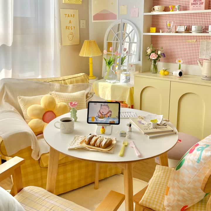 Bright yellow and white toned compact home cafe space featuring cozy cushions and a central round table with personal gadgets
