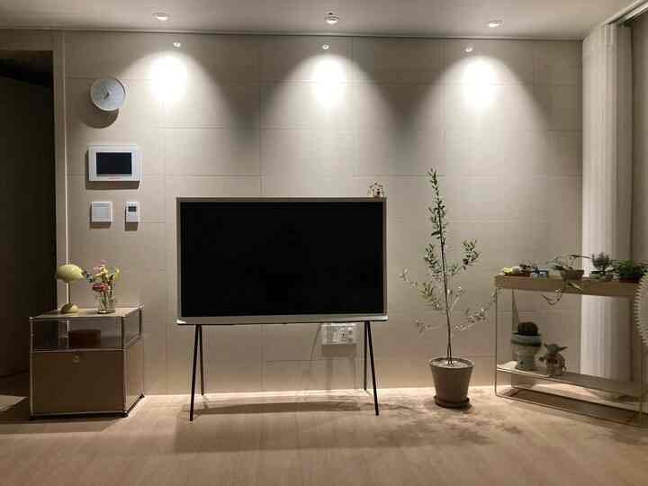 ベージュトーンのリビング、大型ネイビーテレビ台とシンプルモダンな家具、植物が配置された落ち着いた空間