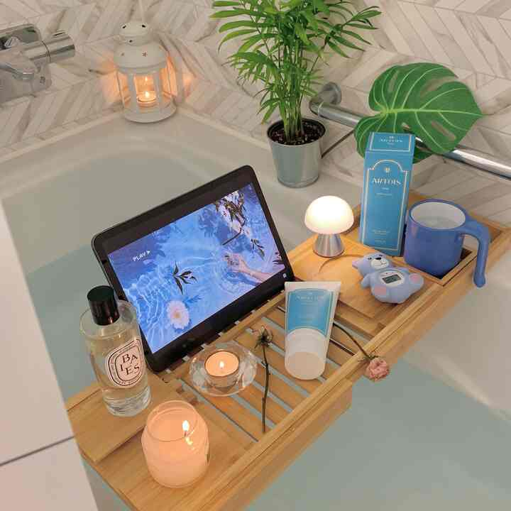 白と青のトーンのバスルーム、浴槽上の木製トレイにキャンドル、デジタル温度計、LEDランプが配置された落ち着いた半身浴空間