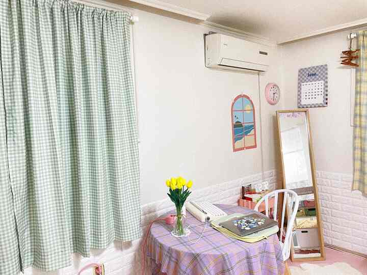淡いグリーンとイエローのチェックカーテンがあるコンパクトな一人暮らしの部屋、デスクや鏡、黄色のチューリップの花瓶が配置された居心地の良い空間