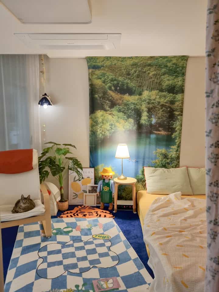Pastel and blue toned bedroom featuring DIY lighting, a cat on armchair, and decorative accessories creating cozy ambiance