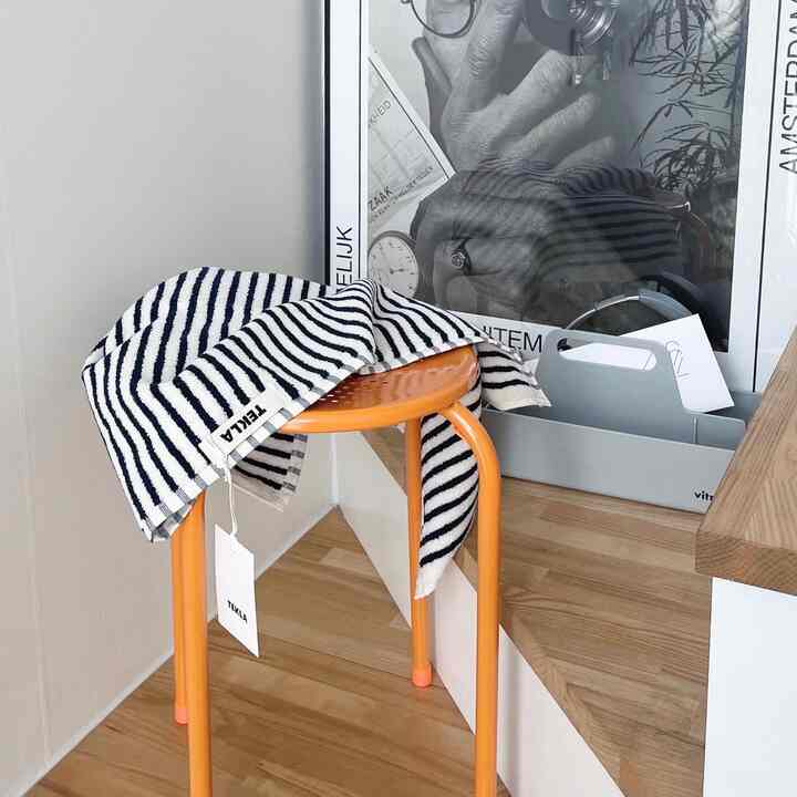 Modern corner space with an orange stool draped with a white striped towel, wood tone flooring, and white walls