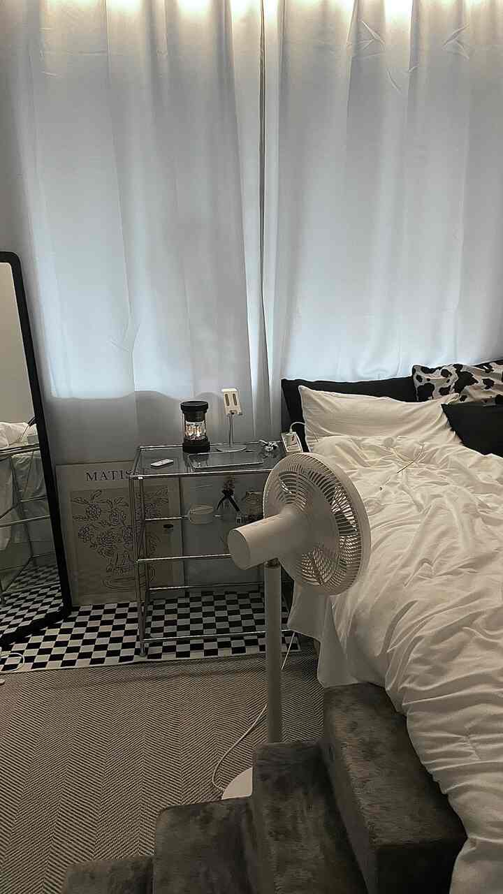 Monotone bedroom in white and black tones featuring a white bed, curtains, shelving, and side table in a clean setup