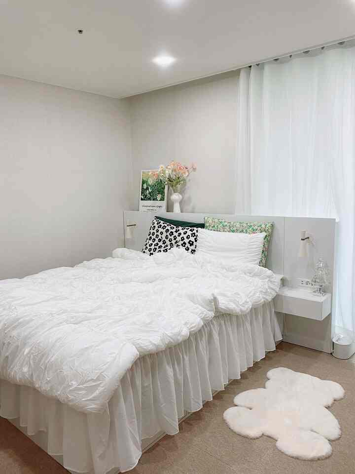 Soft white-toned bedroom featuring a hotel-style bed with shirred bedding and patterned pillows, creating a cozy atmosphere