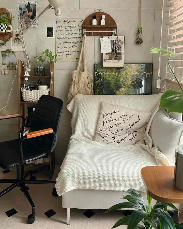 Small living room in ivory and beige tones featuring simple modern sofa, black office chair, wooden shelf, and plants creating a cozy atmosphere