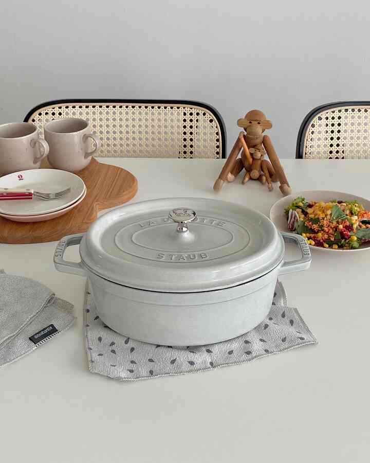 白と木目調のリビング、リビングテーブルの上にスタウブの鍋や皿、カップ、カトラリーが置かれた雰囲気のあるホームクッキング空間