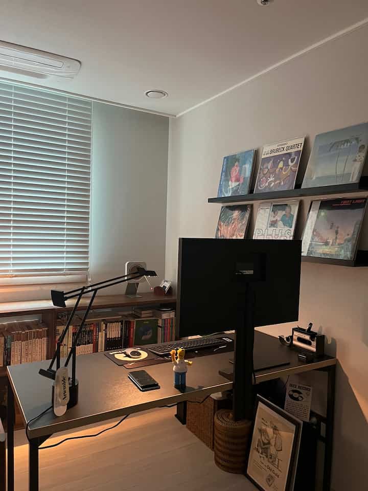 A walnut and black toned study featuring a desk, wall-mounted shelves with LP records and books, showcasing a modern and tidy atmosphere