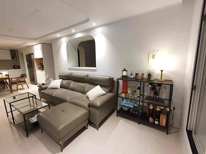 白いトーンのリビング、モダンなリクライニングソファと黒のホームバーキャビネットが配置され、清潔感のある照明が印象的な空間