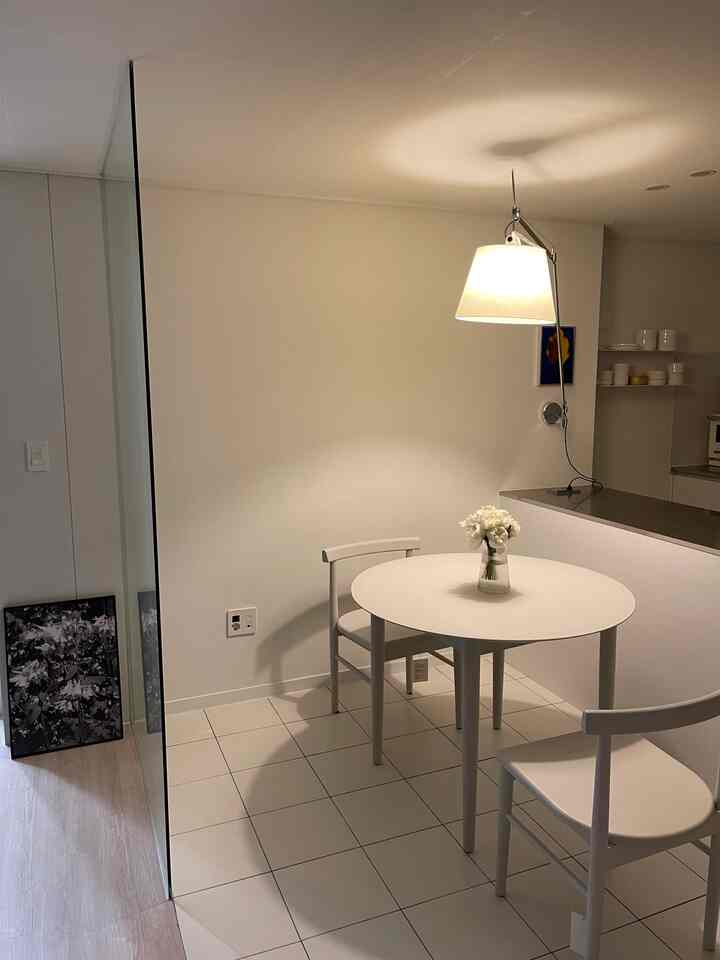 Clean white-toned small dining room featuring a round dining table, two chairs, and a warmly lit pendant lamp for a cozy atmosphere