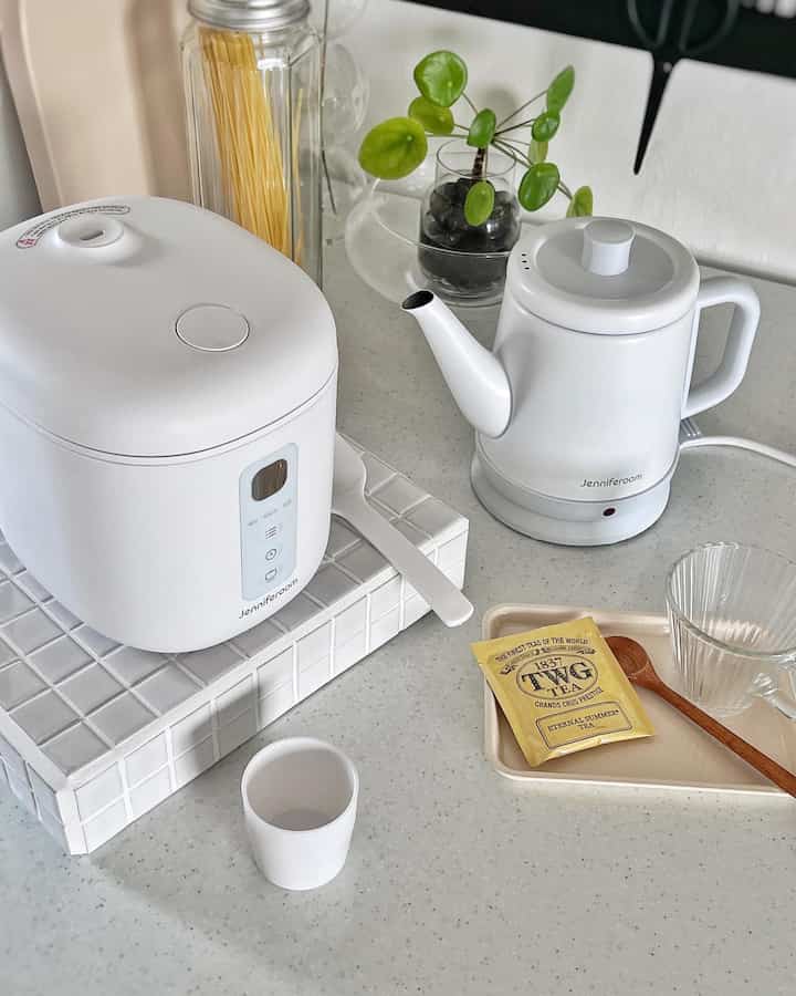 White-toned kitchen space featuring an electric rice cooker, kettle, and cup with a clean minimal interior