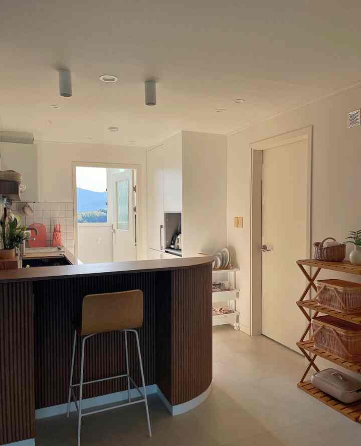 明るいホワイトと濃いウッドトーンのモダンなキッチン、カウンタースツールと収納棚が配置された清潔感のあるインテリア