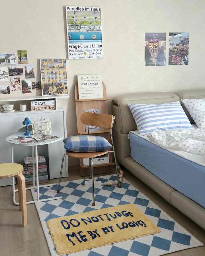 ブルーとアイボリーベージュの調和が美しい寝室、ベッドやサイドテーブル、ラグ、椅子、ポスターが配置された雰囲気のあるおうちカフェインテリア