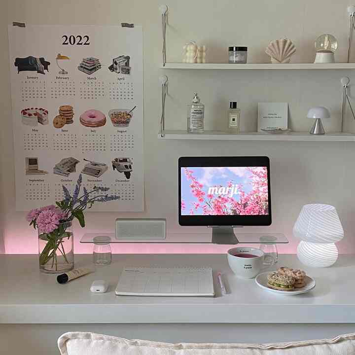 A white and pink toned studio apartment home office featuring a desk and shelves with modern, simple decor, creating a cozy workspace