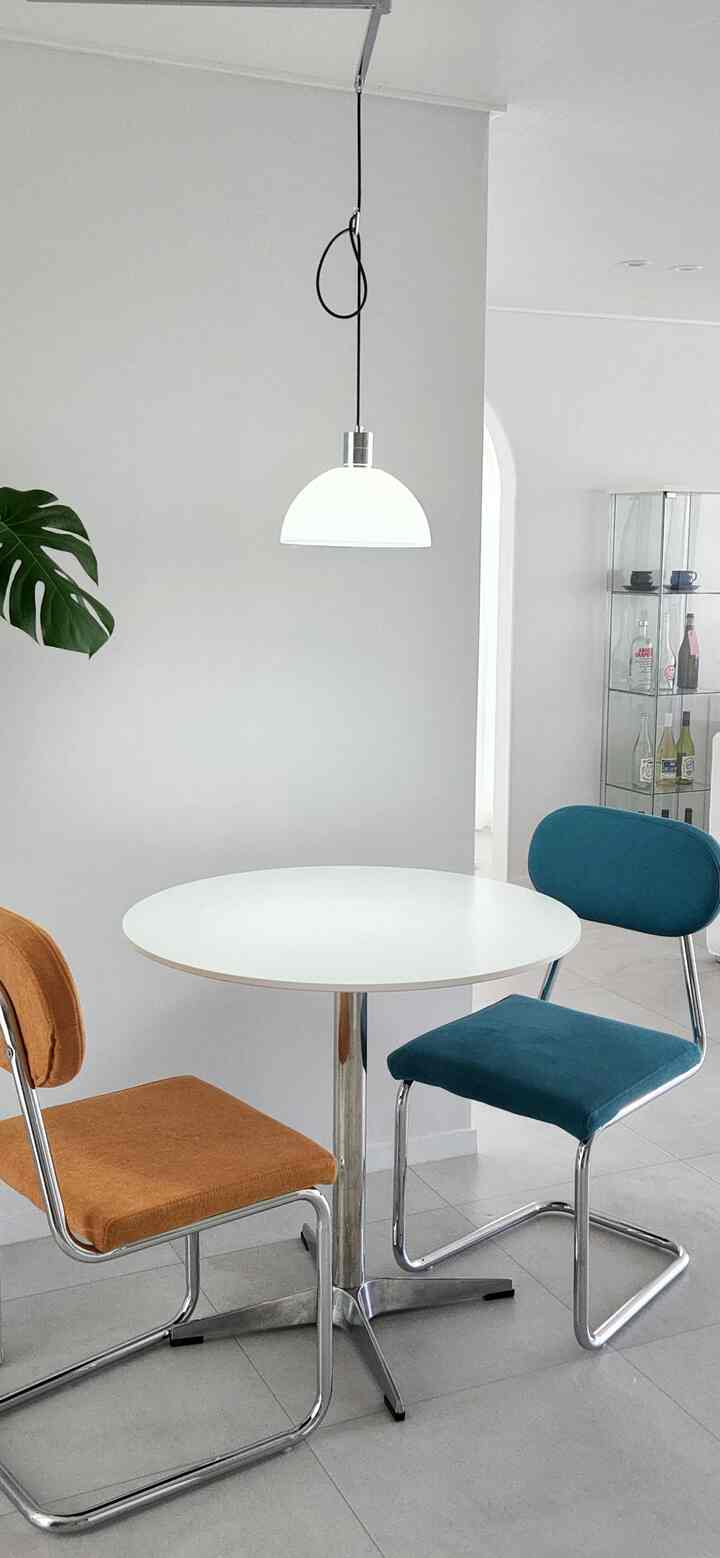 White natural-toned two-person dining space featuring a round table with orange and blue chairs in a minimalist interior