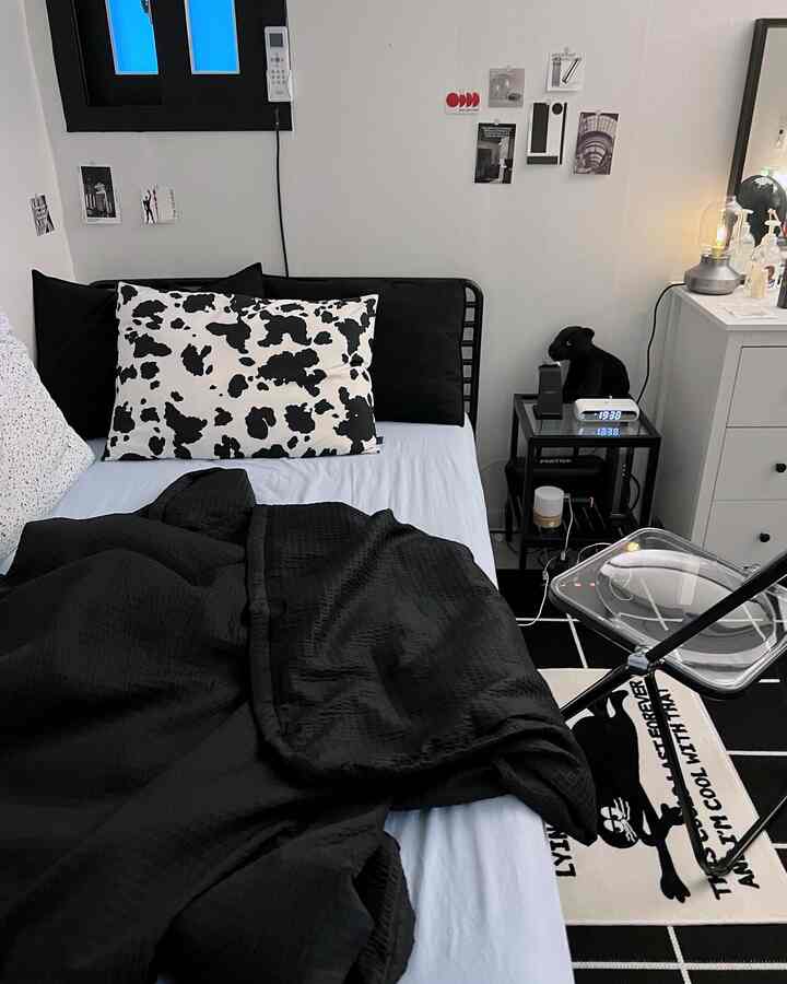 ブラックとブルーのトーンが特徴のワンルーム寝室、中央に黒いベッドと掛け布団、柄付き枕が配置されたモダンなインテリア