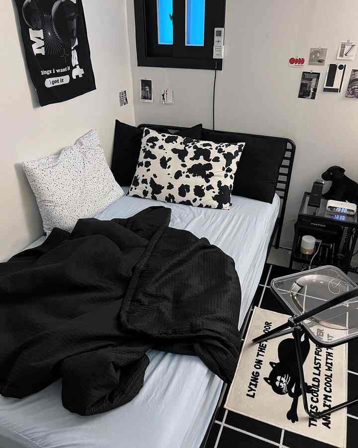 Black and white toned bedroom featuring a black bed frame and bedding, transparent chair and rug in a modern setting